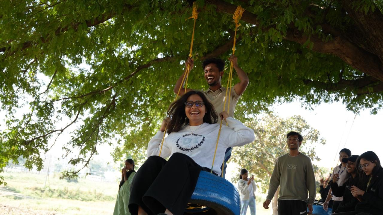 Students playing on a tyre swing under a large campus tree